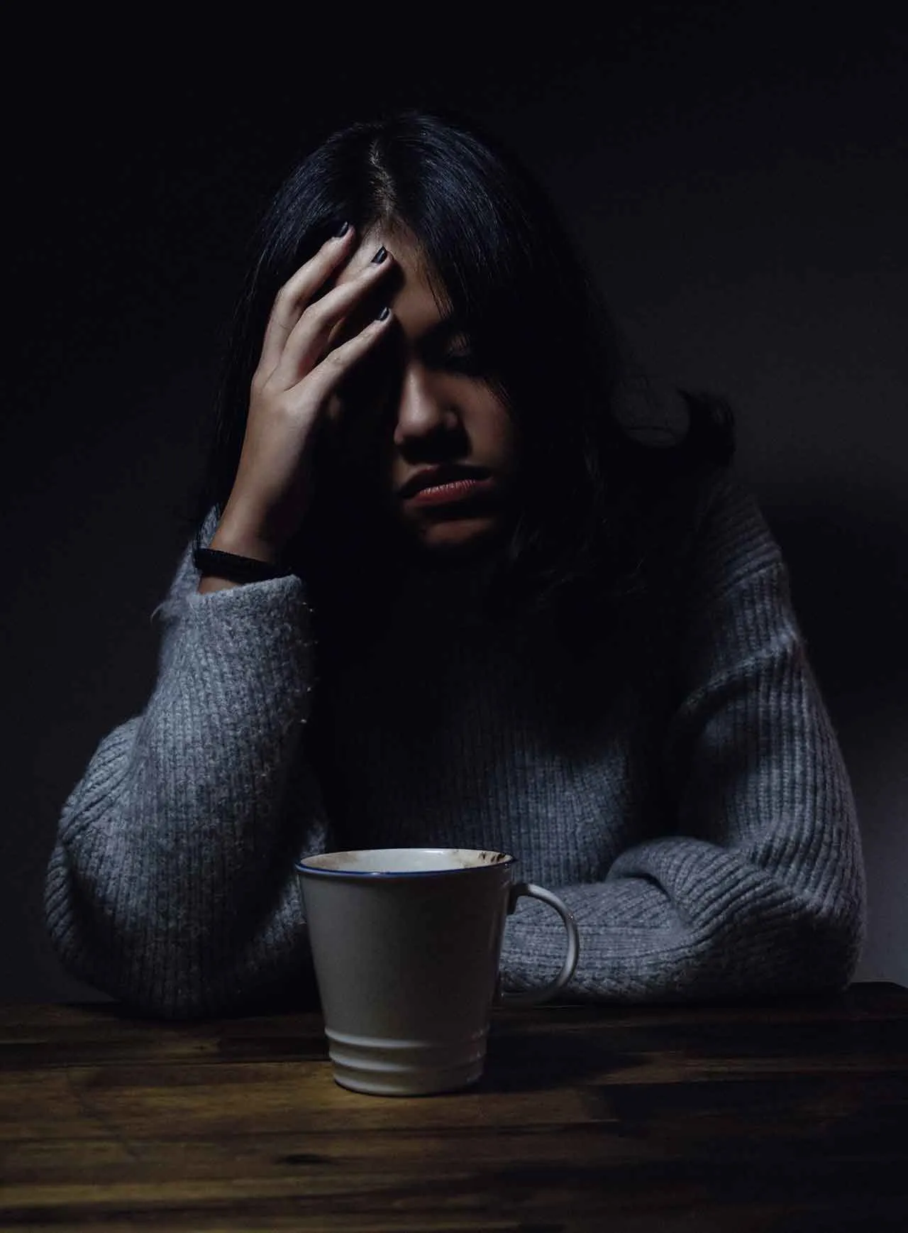 A woman with phone anxiety sitting at a table, head in her hands.