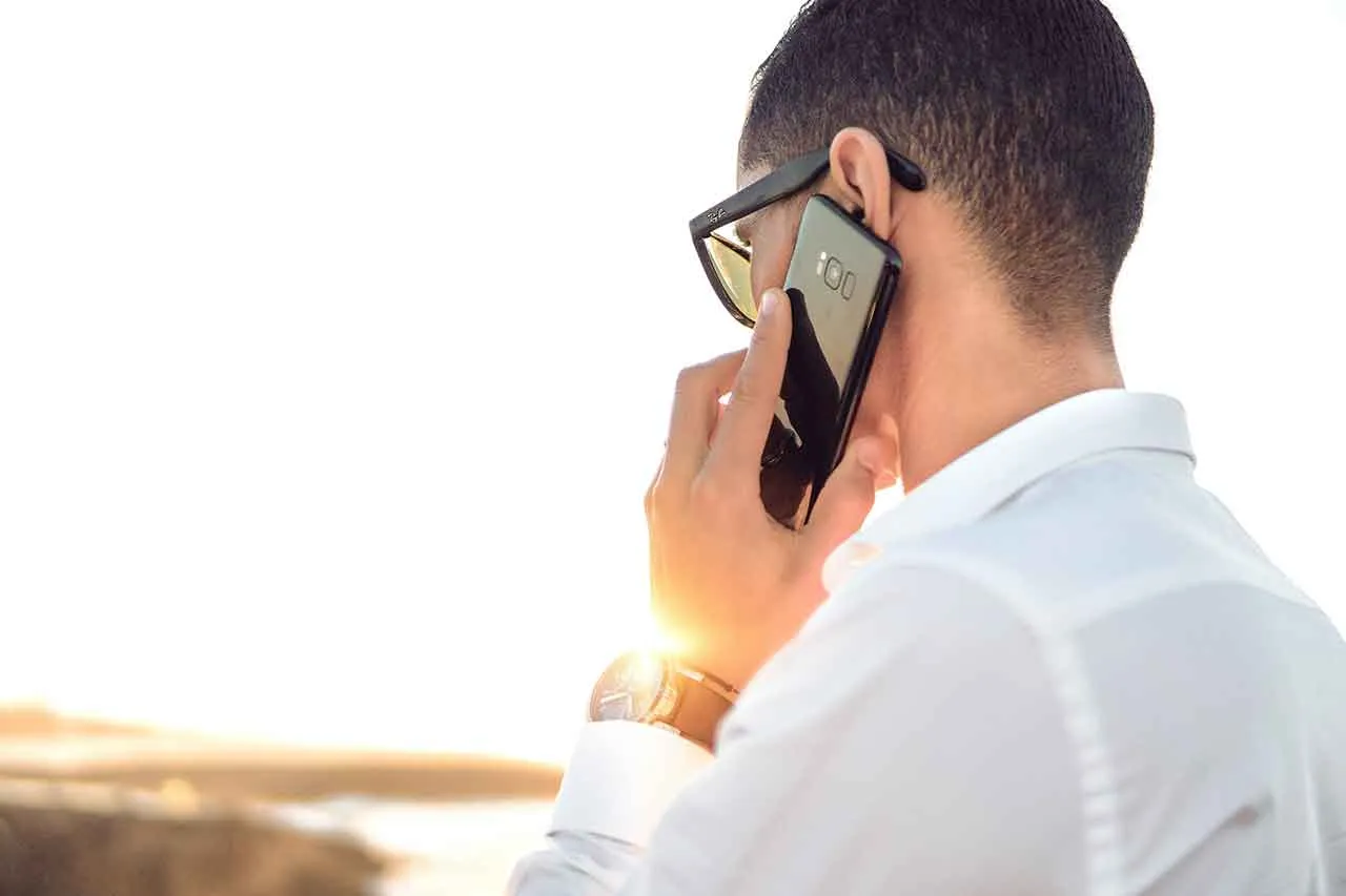 A man on the beach on the phone, listening with anxiety.