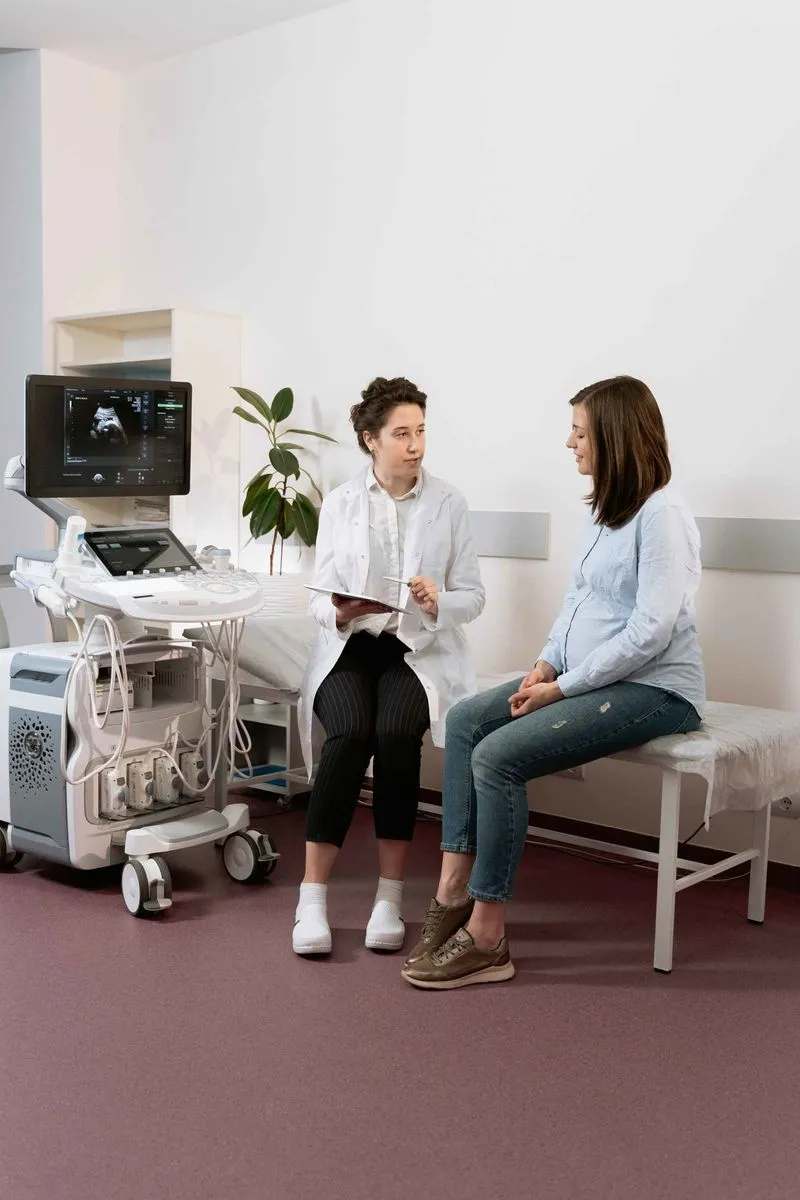 Doctor with a clipboard talking to a pregnant woman seated beside an ultrasound machine