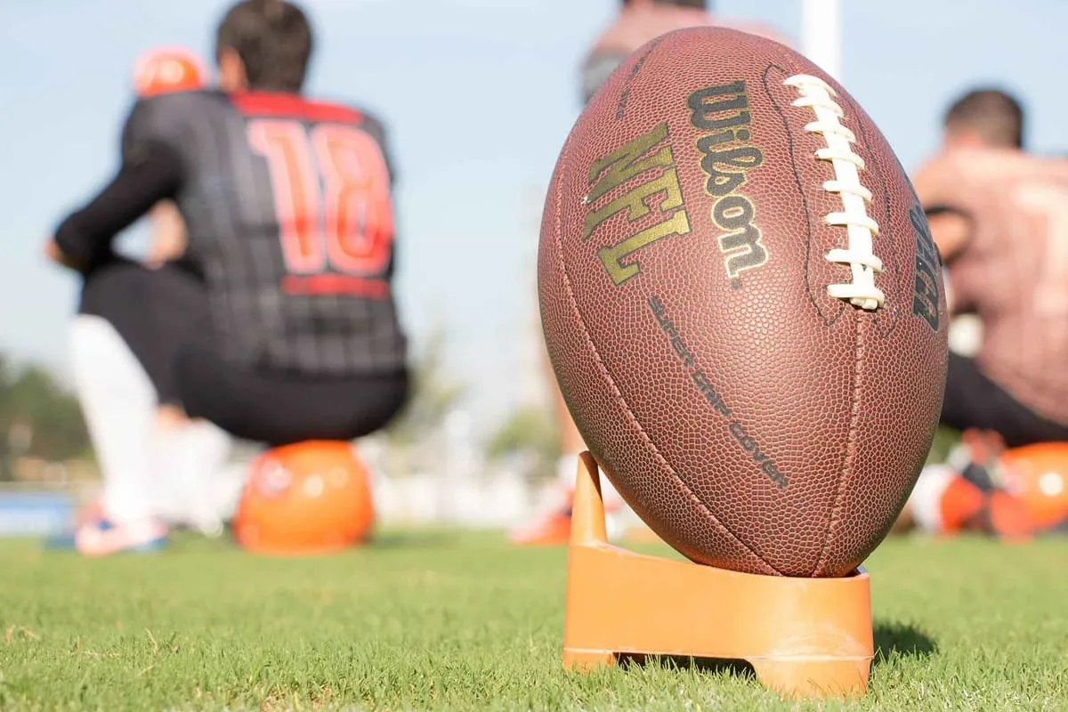 Wilson NFL football on an orange kicking tee with players blurred in the background