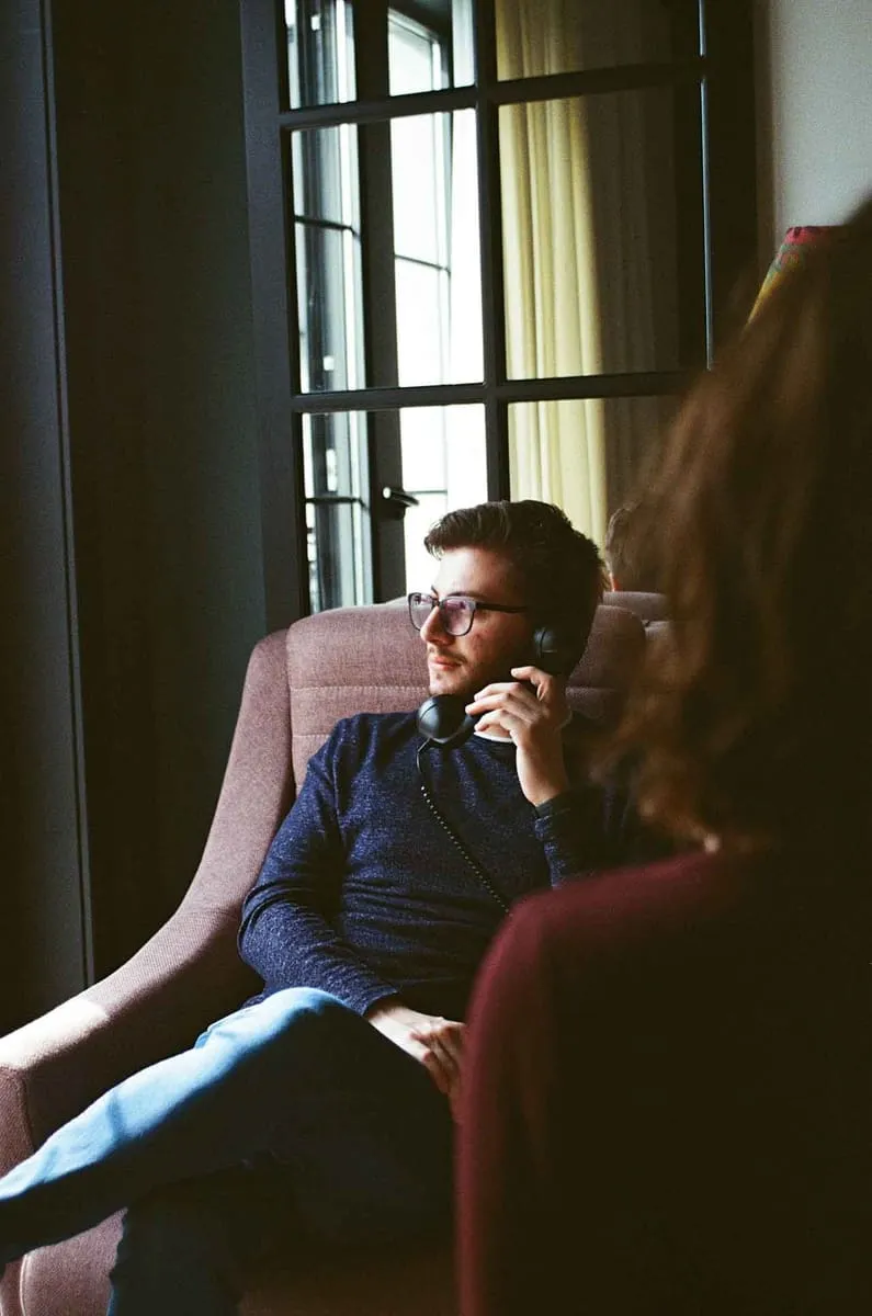 A man with phone anxiety, sitting on the couch, listening attentively on the phone.