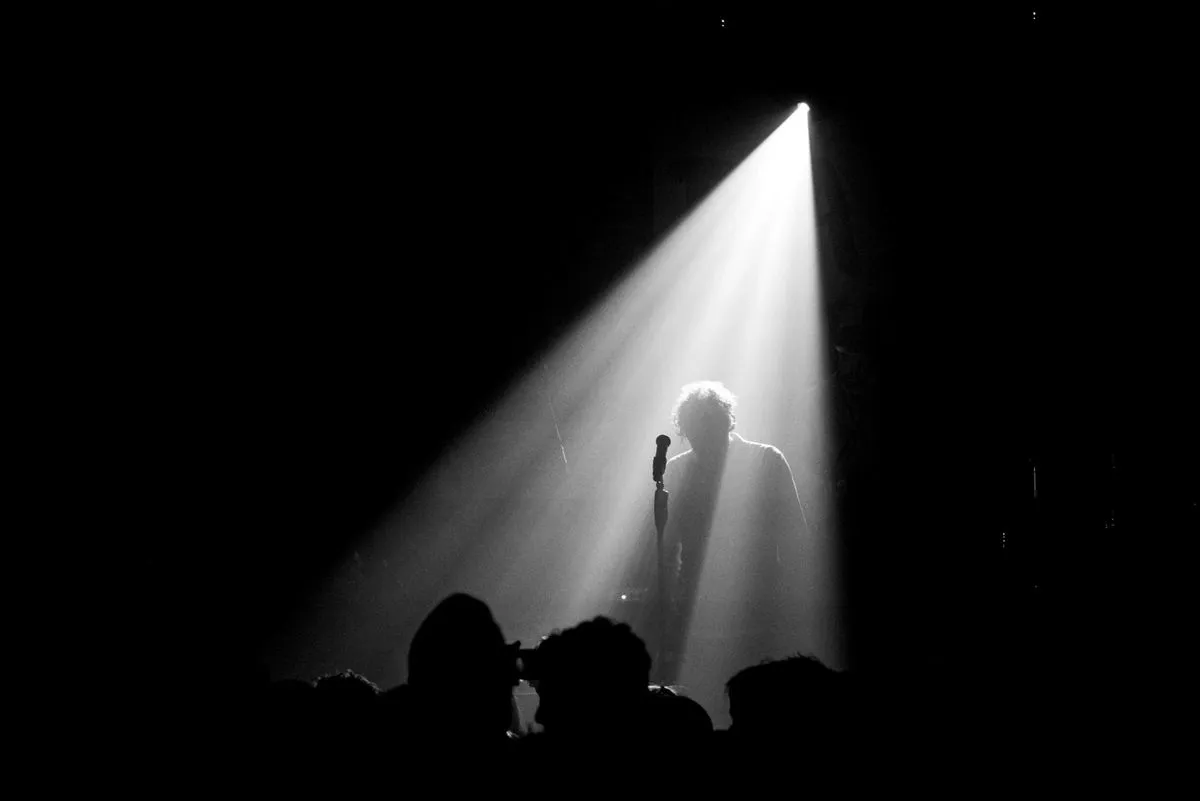 Silhouette of a singer standing at a microphone under a single spotlight on a dark stage