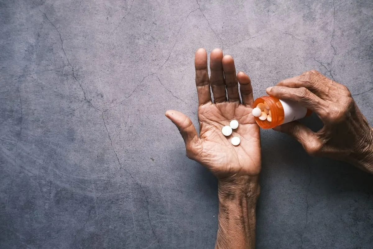 A pair of old hands pouring pills into one hand.